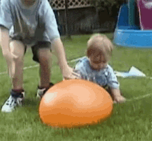 a boy and a baby are playing with an orange ball