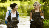 two women in waders are standing next to each other in a lake .