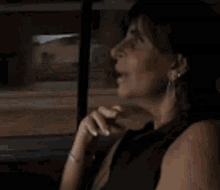 a woman is sitting in a car looking out the window and making a peace sign with her hand .
