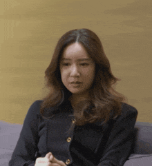 a woman in a black sweater with gold buttons sits on a couch