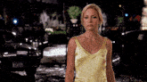 a woman in a yellow tank top is standing in front of a black car with a license plate that says e7xs