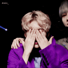 a man in a purple jacket covering his eyes with his hands