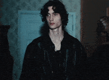 a man with curly hair wearing a black leather jacket and a necklace