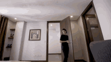 a woman opens a door in a bedroom with a framed picture on the wall that says ' always '