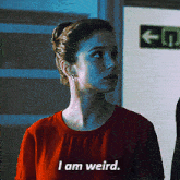 a woman in a red shirt says i am weird in front of a green exit sign