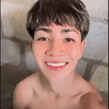 a shirtless young man is taking a selfie in a bathroom and smiling .