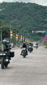 a group of motorcycle riders are riding down a street with a sign that says i love cambodia