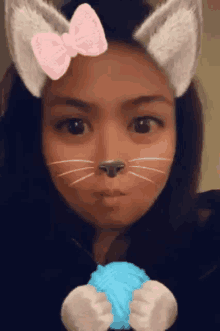 a woman wearing cat ears and a pink bow on her head is holding a ball of yarn .