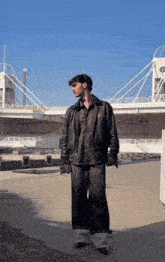 a man in a leather jacket stands in front of a white bridge