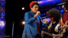 a woman sings into a microphone while a man plays a guitar in front of a nbc screen