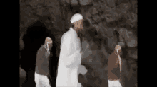 a man in a white robe is standing in a cave with two other people .