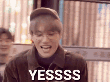 a young man wearing glasses and a hat is laughing and saying yesss .