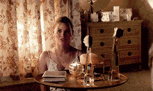 a woman is sitting at a table in a room with a dresser in the background