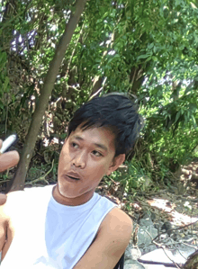 a man in a white tank top is sitting in a chair in the woods