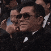 a man wearing sunglasses sits next to a woman