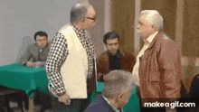 a group of men are standing around a table talking to each other in a room .