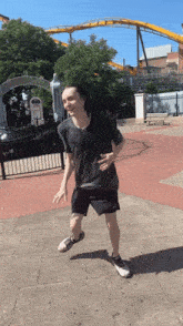 a man in a black shirt and black shorts is dancing in front of a roller coaster
