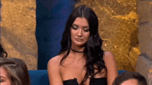 a woman in a black dress is sitting in a crowd of people and looking at the camera .