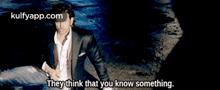 a man in a suit and white shirt is sitting on the ground with the words `` they think that you know something '' .