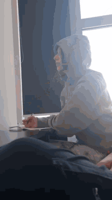 a person wearing a grey hoodie is sitting at a desk with a laptop