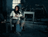 a woman is sitting in a chair in a dark room with a man in the background