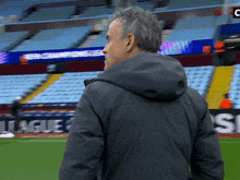 a man in a grey jacket stands on a soccer field