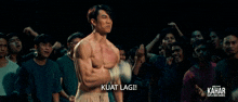 a man without a shirt is standing in front of a crowd and the caption kuat lagi