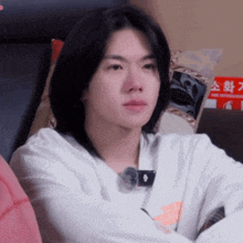 a young man with long black hair is sitting on a bed with a pillow that says fire extinguisher on it