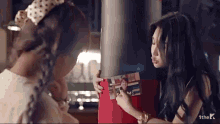two women are standing next to each other and one of them is holding a red box with a picture of a woman on it ..