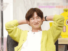 a man wearing a yellow cardigan is sitting in a chair with his hands behind his head