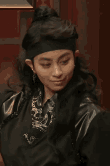a woman wearing a headband and a ring is pointing at herself