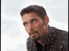 a man with a beard and earrings is wearing a black jacket and earrings .