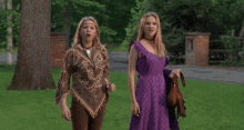 two women in purple dresses are dancing in a grassy field