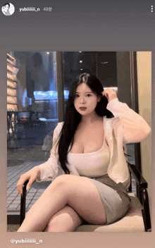 a woman in a white tank top sits in a chair with her legs crossed in front of a window ..