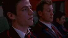 two men in suits and ties are sitting in a dark room