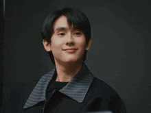 a young man in a black jacket with a striped collar smiles