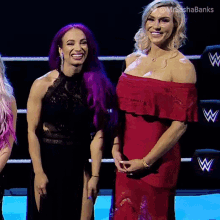a woman with purple hair and a woman in a red dress stand next to each other