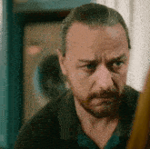 a man with a beard is looking at the camera with a serious look on his face