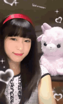 a girl wearing a red headband stands next to a pink stuffed animal