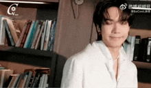 a man in a white shirt is standing in front of a bookshelf with books on it .