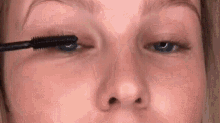 a woman is applying mascara to her eyelashes with a brush .