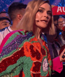 a woman in a colorful jacket is holding a sign that says " all "