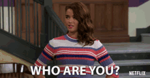 a woman in a striped sweater stands in front of stairs and says " who are you "