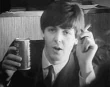 a man in a suit and tie is smoking a cigarette while holding a can of coke .