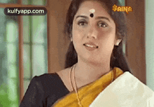 a woman in a yellow saree and black top is smiling .
