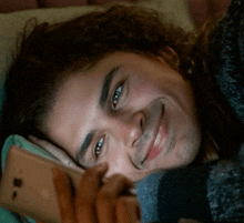 a man with curly hair is smiling while looking at a cell phone