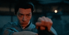 a man in a blue shirt is holding a sword in his hand in the dark .