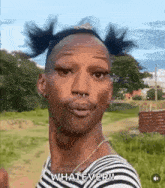 a man with pigtails and a nose ring is standing in a field and making a funny face .
