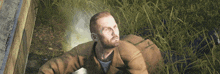 a man in a brown jacket sits in a field of tall grass