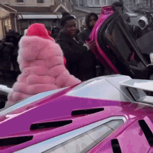 a woman in a pink fur coat is standing next to a pink car .